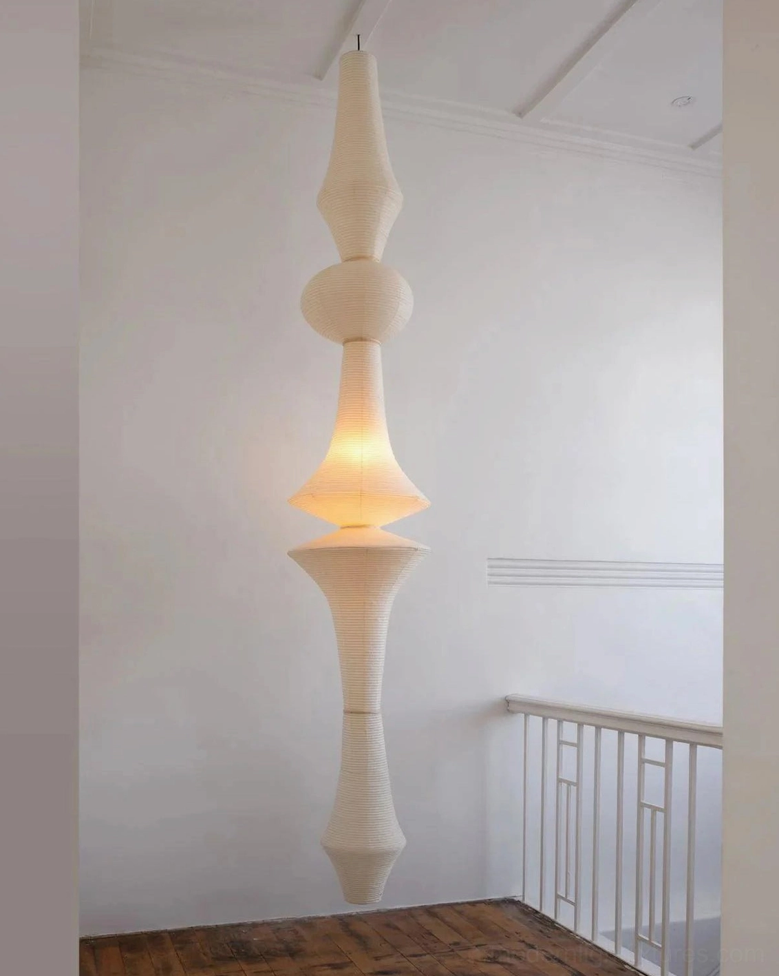 Tall Akari E tapered white paper pendant lamp in modern home stairwell landing with warm glowing light