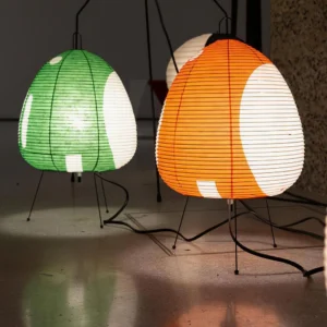Illuminated Akari table lamps in green and orange tones casting warm glowing light on concrete floor indoor setting