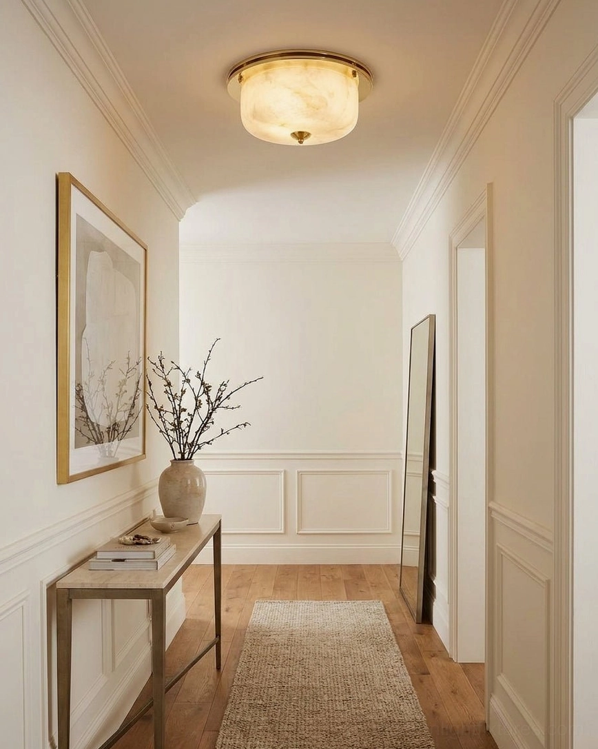 Justice alabaster ceiling fixture illuminating traditional hallway with wainscoting, console table, and wall art