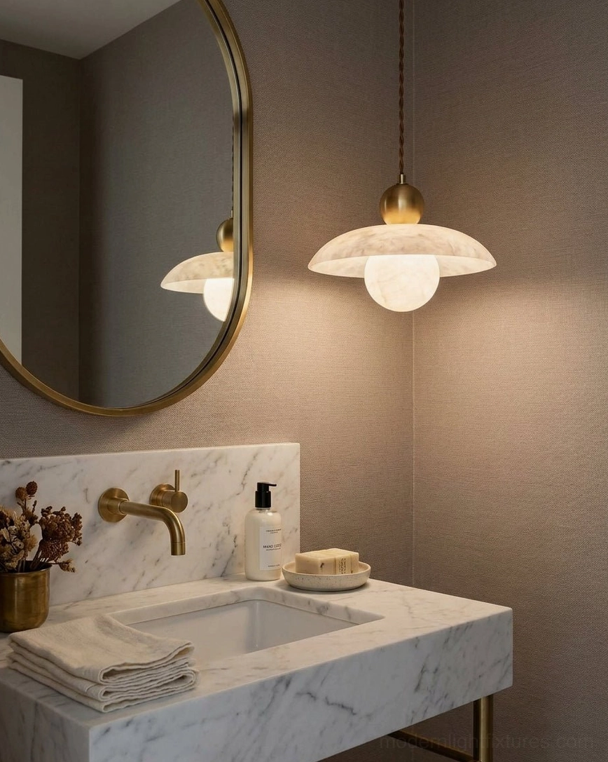 Alabaster pendant light hanging above bathroom vanity with round mirror, warm brass fixtures, and neutral tile backdrop