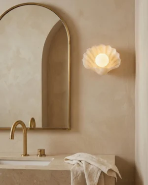 Alabaster seashell wall sconce mounted above bathroom vanity with warm coastal lighting paired with brass fixtures and neutral marble tile
