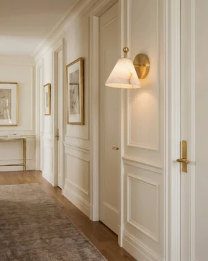 Pair of alabaster wall sconces flanking entry hallway paneled wall, warm brass finish, residential corridor lighting