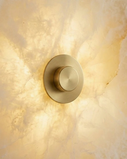 Alabaster wall sconce mounted on blank white wall showing sculptural form and brushed brass center disc