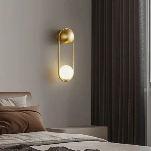 Polished brass Alaynia globe wall sconce illuminated in modern bedroom creating warm ambient bedside lighting above nightstand