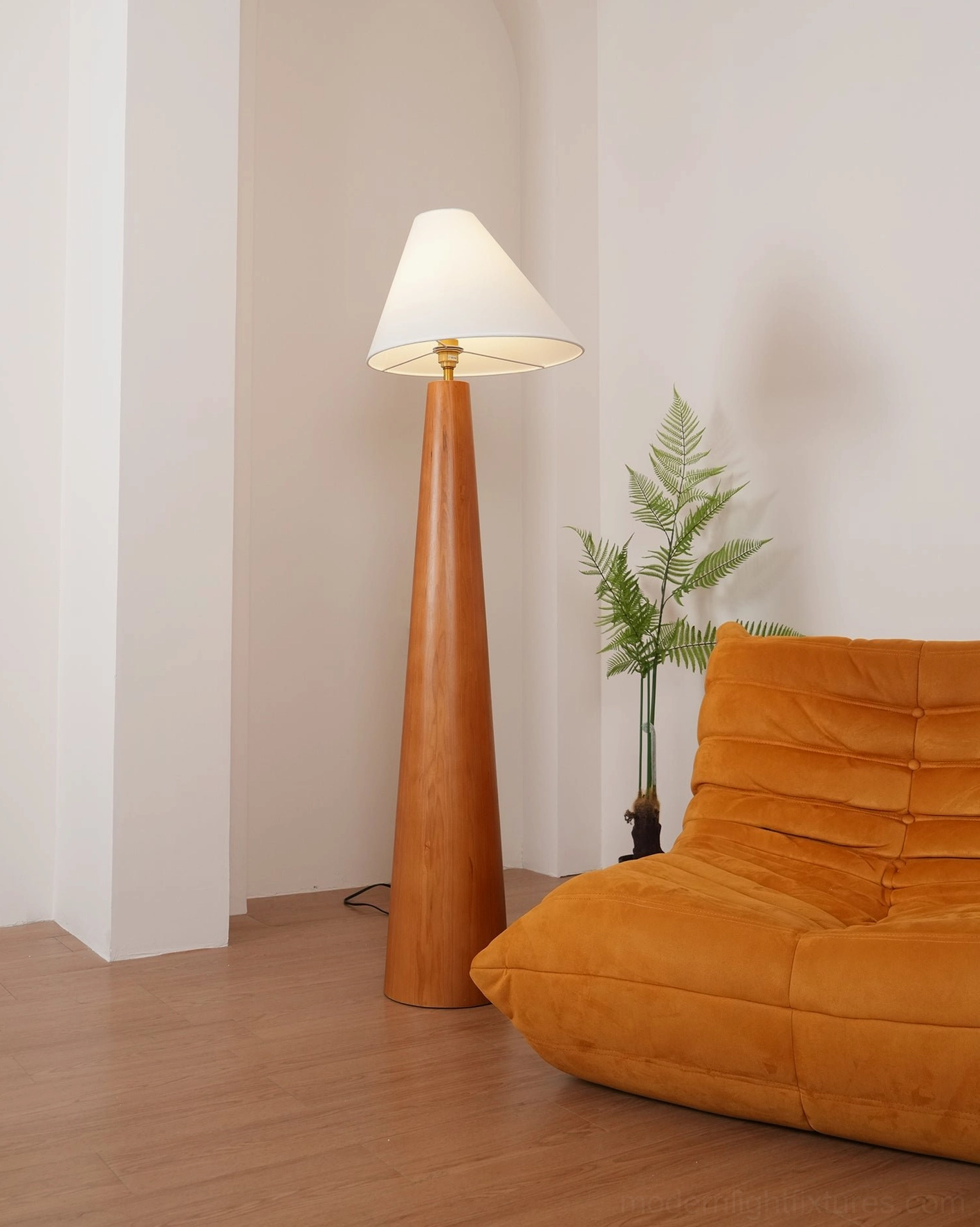 Tapered wood floor lamp with brass base joint displayed in modern living room, three-quarter angle showing warm wood finish and white linen shade