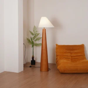 Modern Scandinavian wood floor lamp illuminated in cozy living room setting with wooden floor, tan lounge chair and potted fern, warm soft lighting