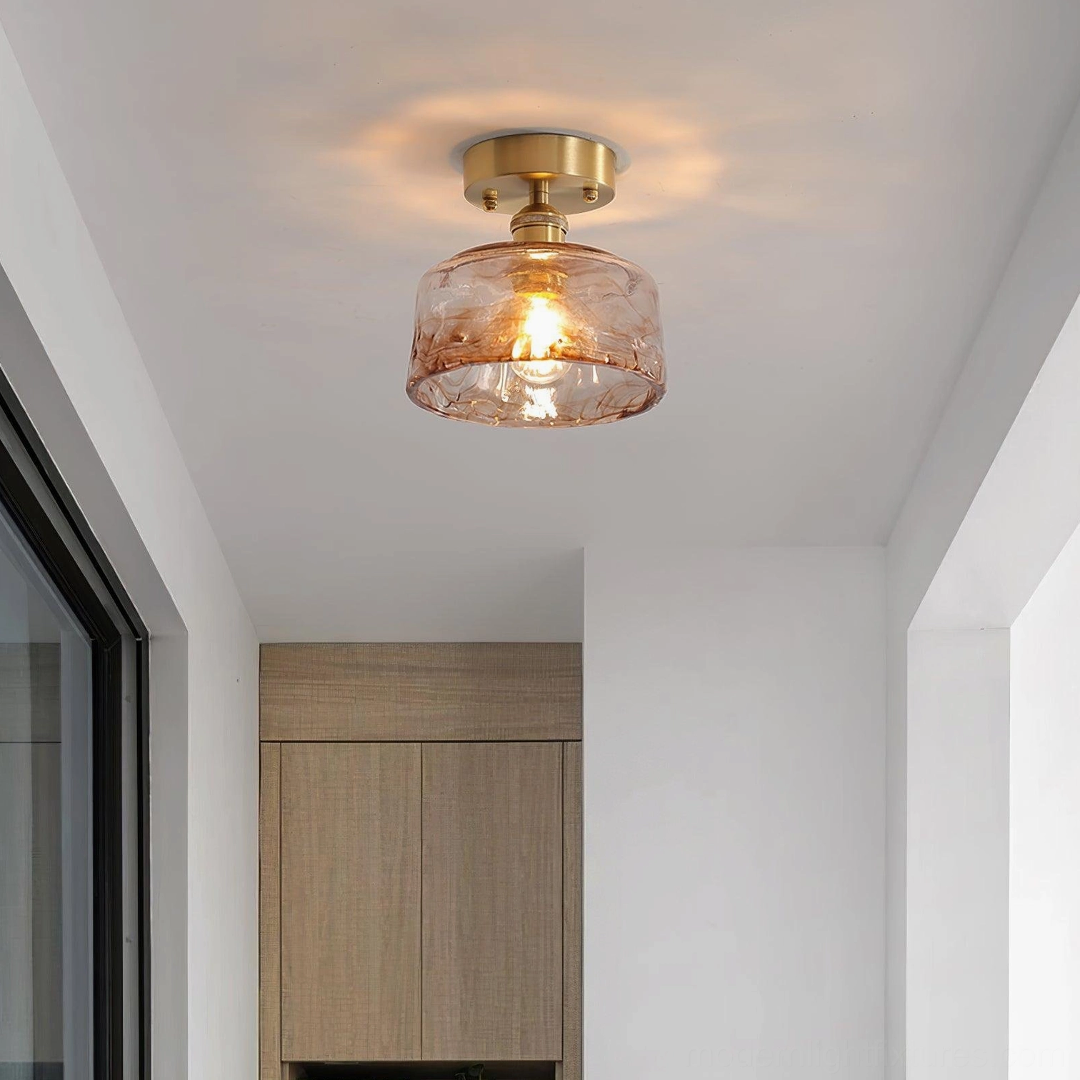Semi-flush amber glass ceiling light with brushed brass base installed above wooden kitchen cabinets, showing warm textured glass