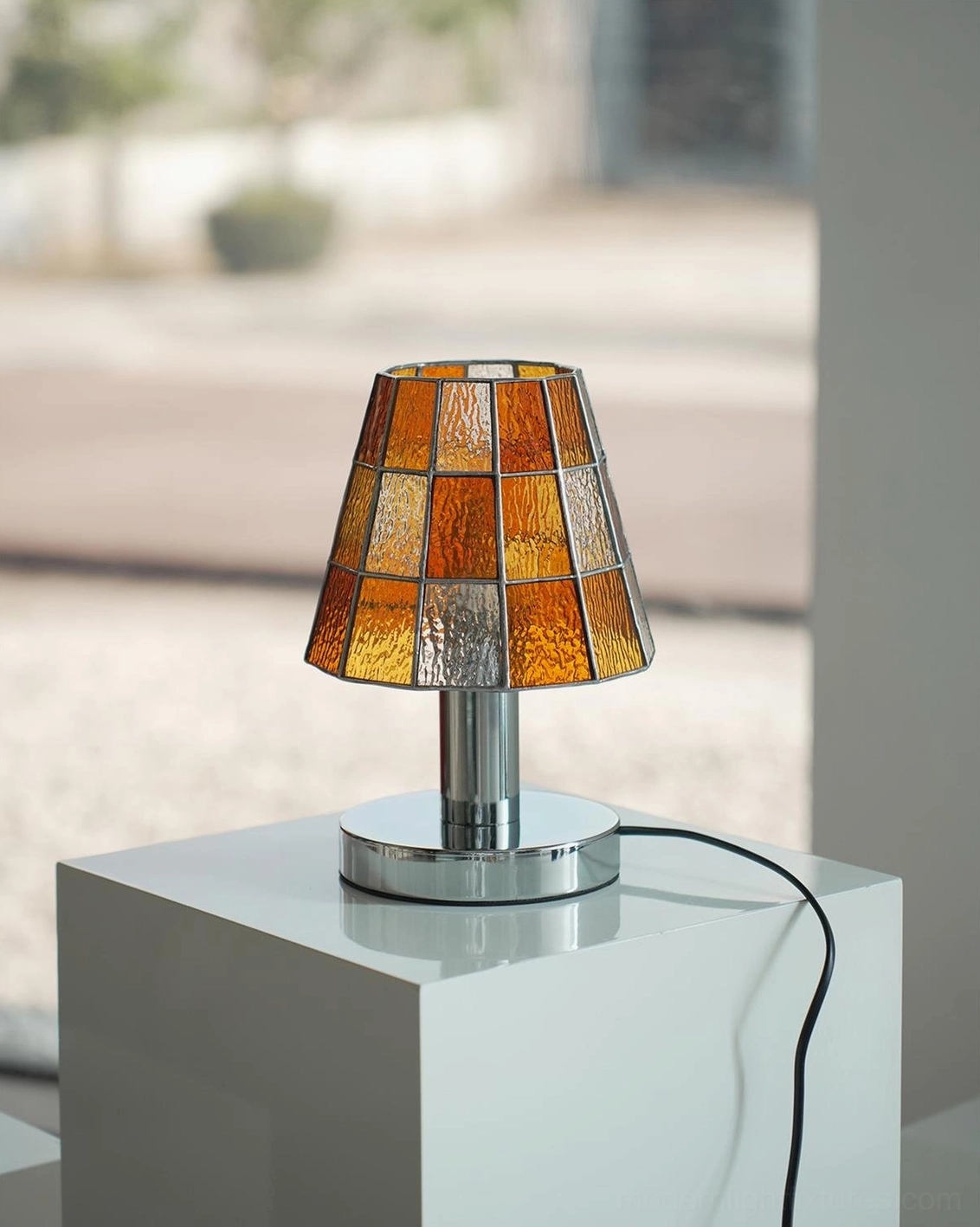 Warm amber-orange stained glass table lamp with chrome base creating glowing ambient lighting