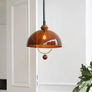 Mid-century modern amber glass pendant lamp hanging in interior space, three-quarter view with white paneled door and green plant decor