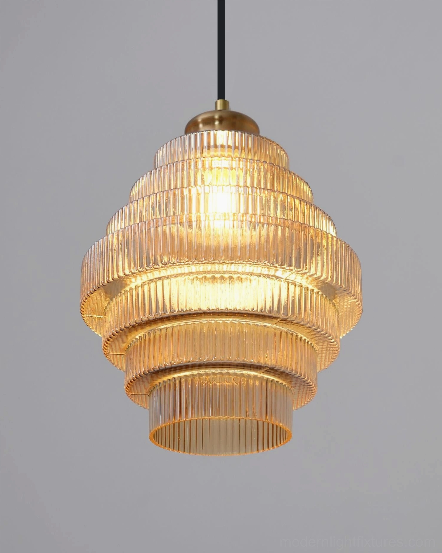 Close-up of illuminated amber ridged glass pendant, showing tiered glass refraction and brass hardware