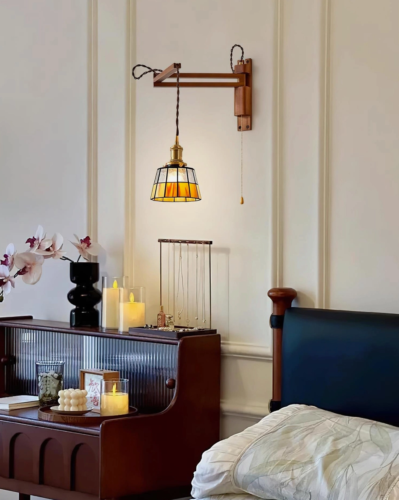 Amber stained glass wall sconce mounted above wooden bedside table in vintage-inspired bedroom interior with warm ambient lighting casting decorative patterns