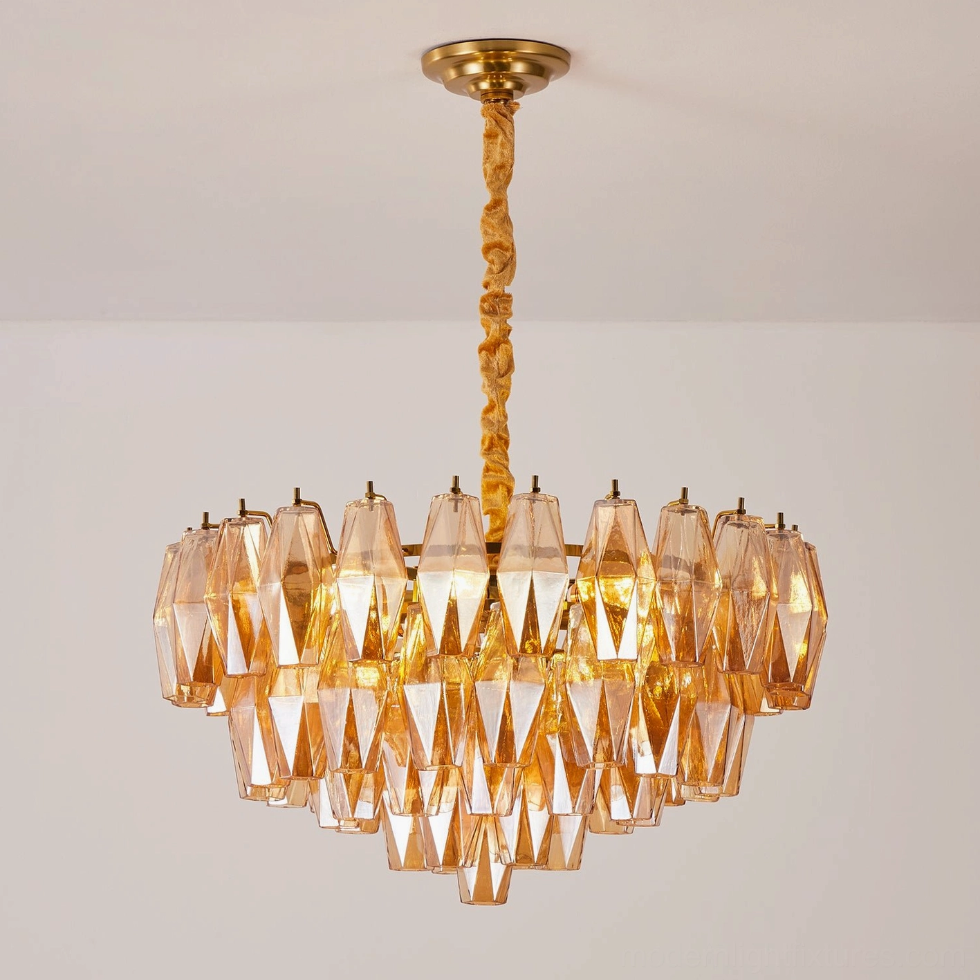 Amber hand-blown glass tiered chandelier illuminated with warm glowing light in interior setting