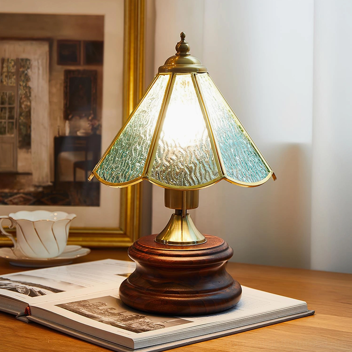 Blue-green aqua stained glass table lamp with rippled texture and gold brass trim, vintage dining table scene with teacup and framed art