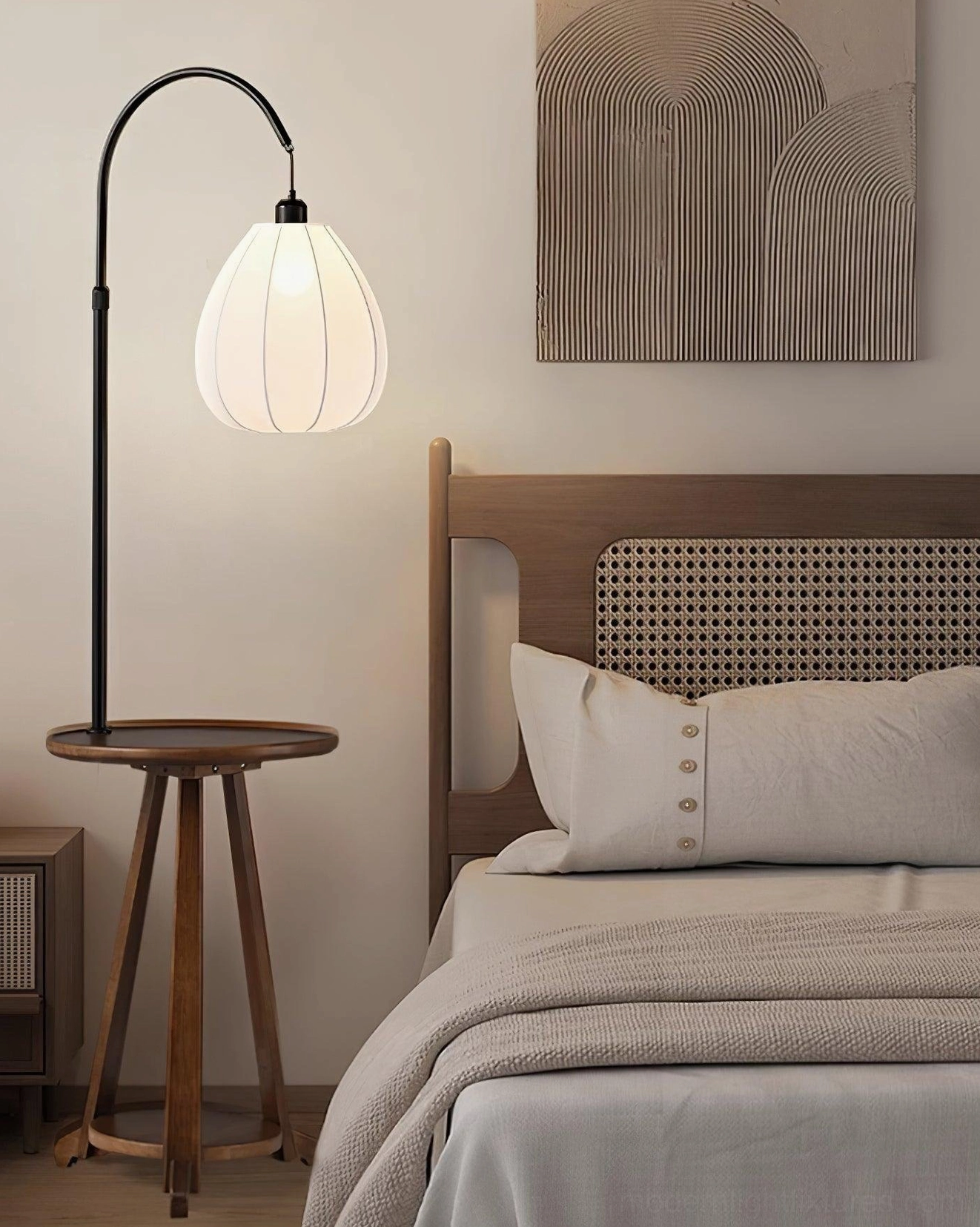 Arc floor lamp with side table positioned in bedroom, woven headboard, neutral linen bedding, wall art decor