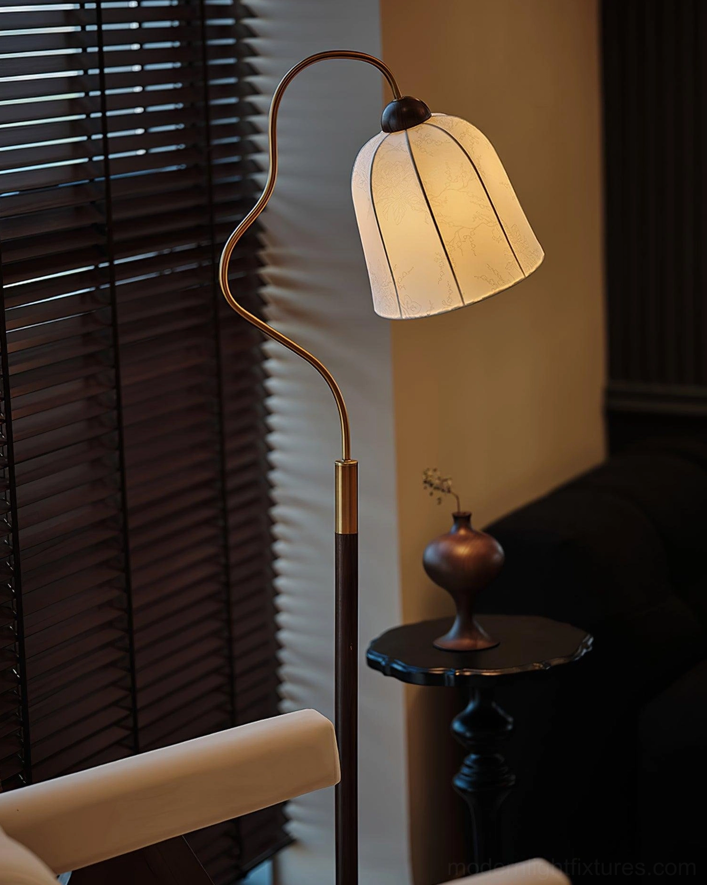 Close-up side view of arc floor lamp with brass detailed walnut pole and glowing beige fabric shade