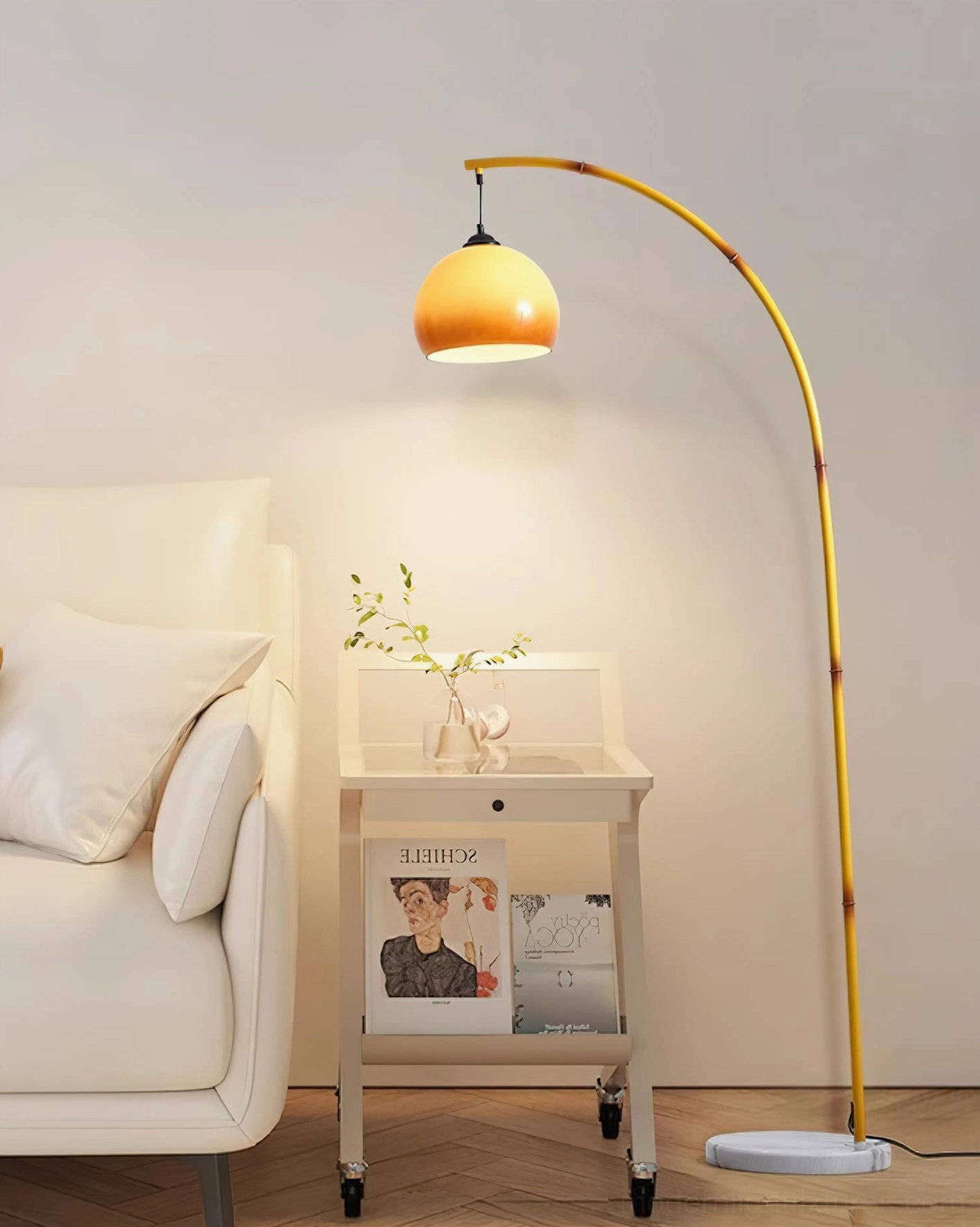 Contemporary arc floor lamp with light yellow pole and caramel glass dome in styled living room with sofa and rolling side table