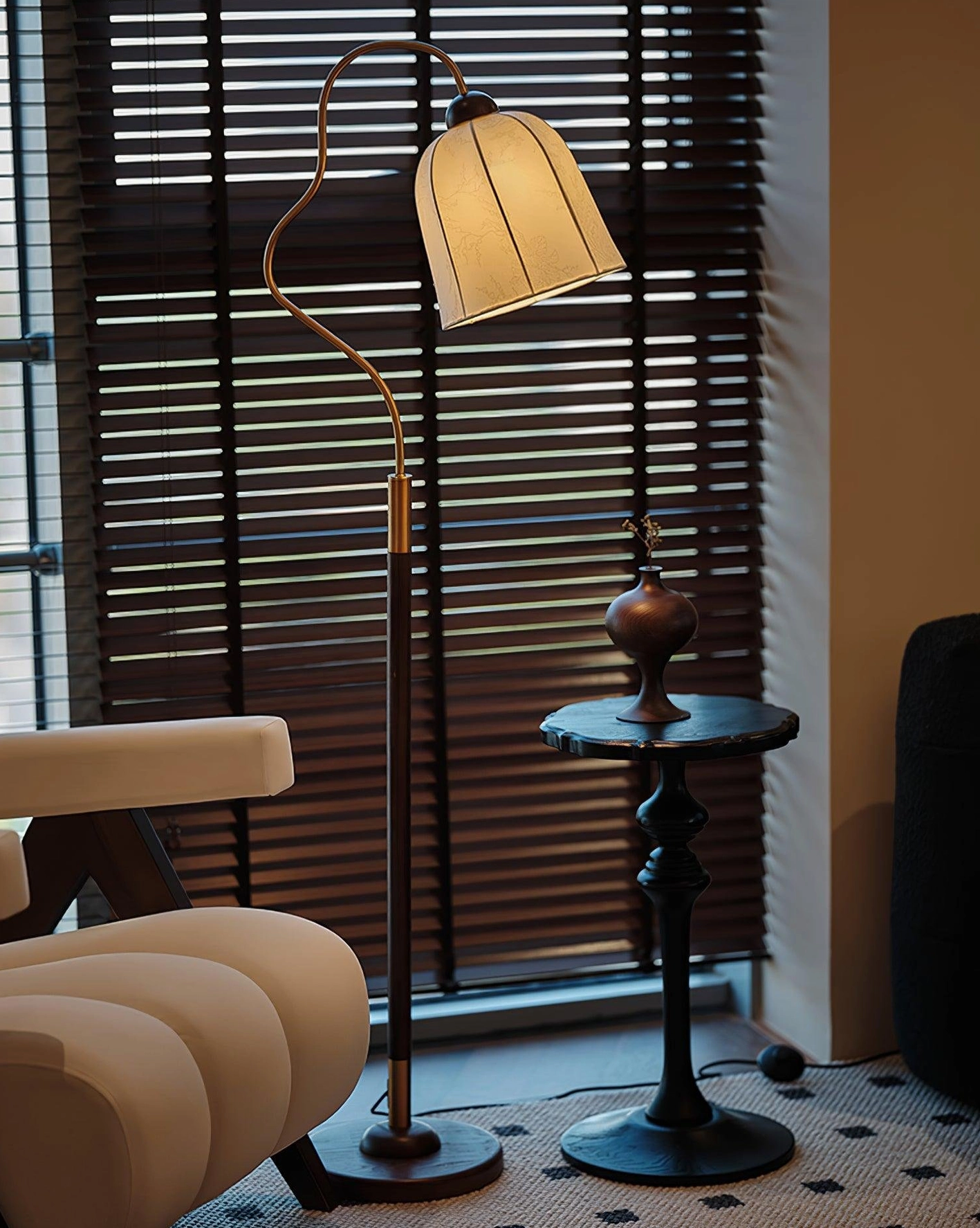 Arc floor lamp in living room with window blinds and side table, black metal pole with brass trim