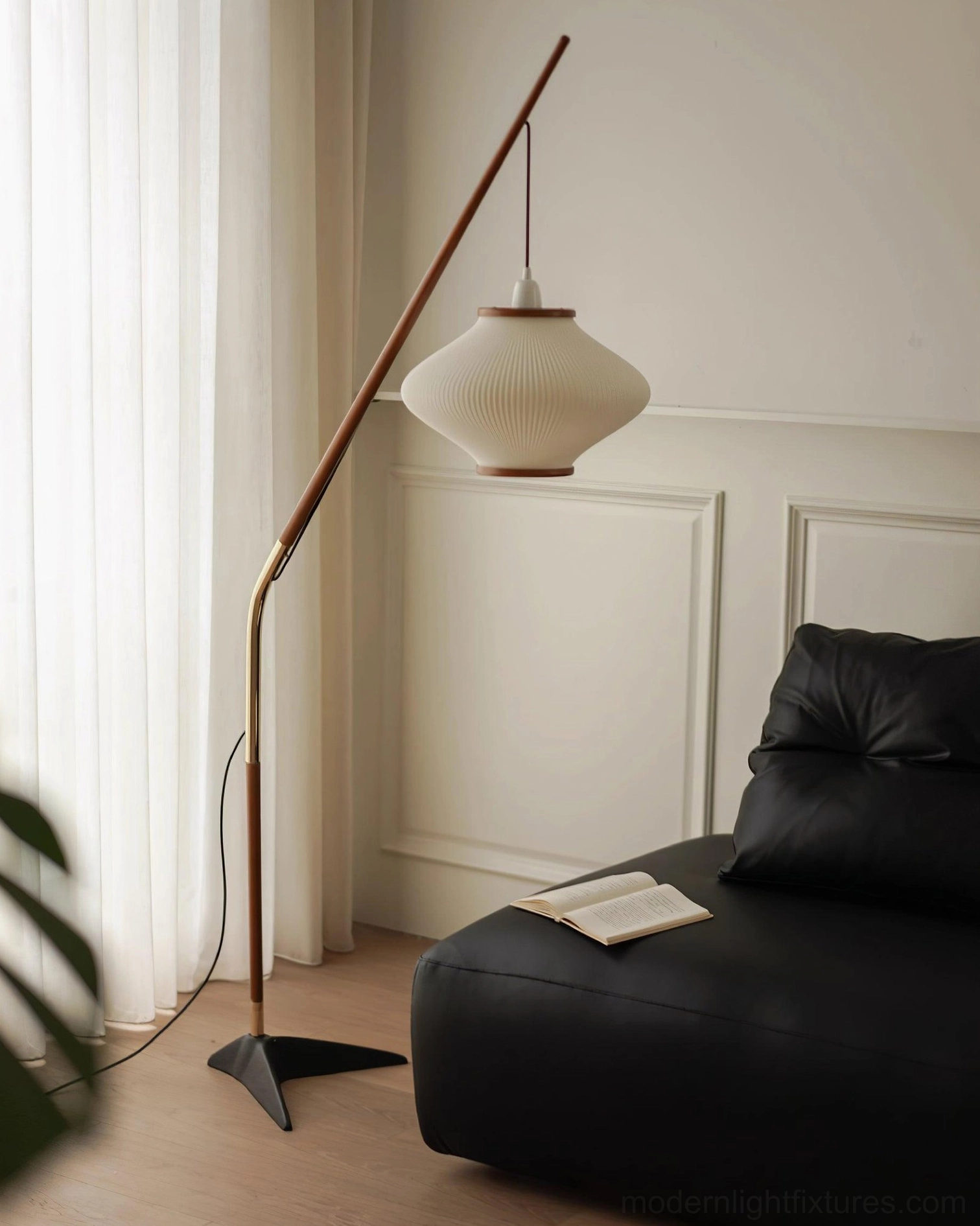 Contemporary arc floor lamp beside black leather sofa and white paneled wall, minimalist interior design