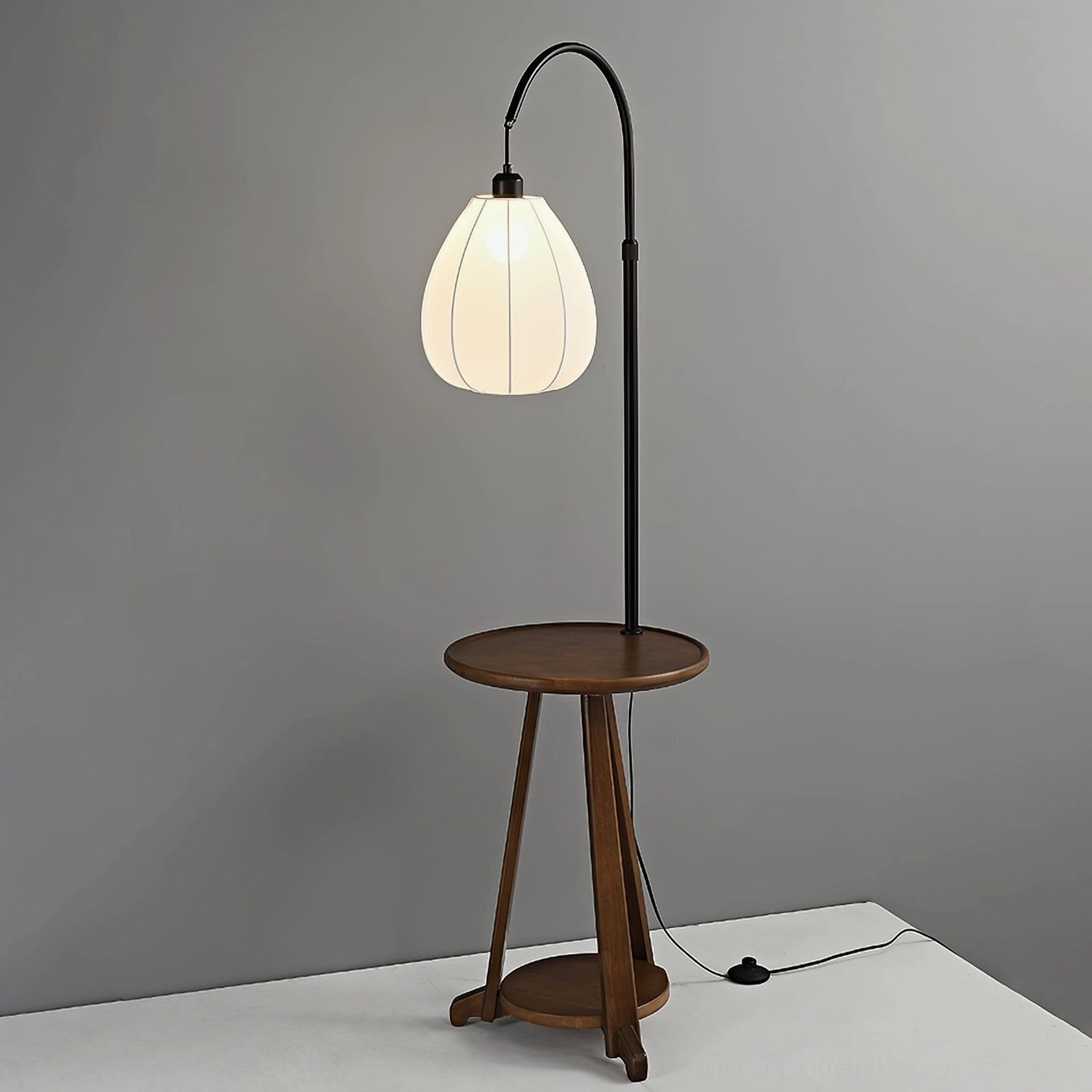 Arc floor lamp with wooden side table and lower shelf, grey studio background, black power cord visible