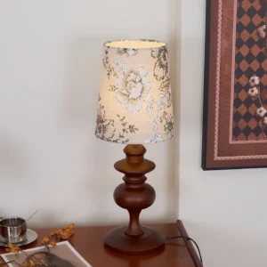 Ariana bedside table lamp in bedroom setting, shown on nightstand with wall art decor for ambient lighting