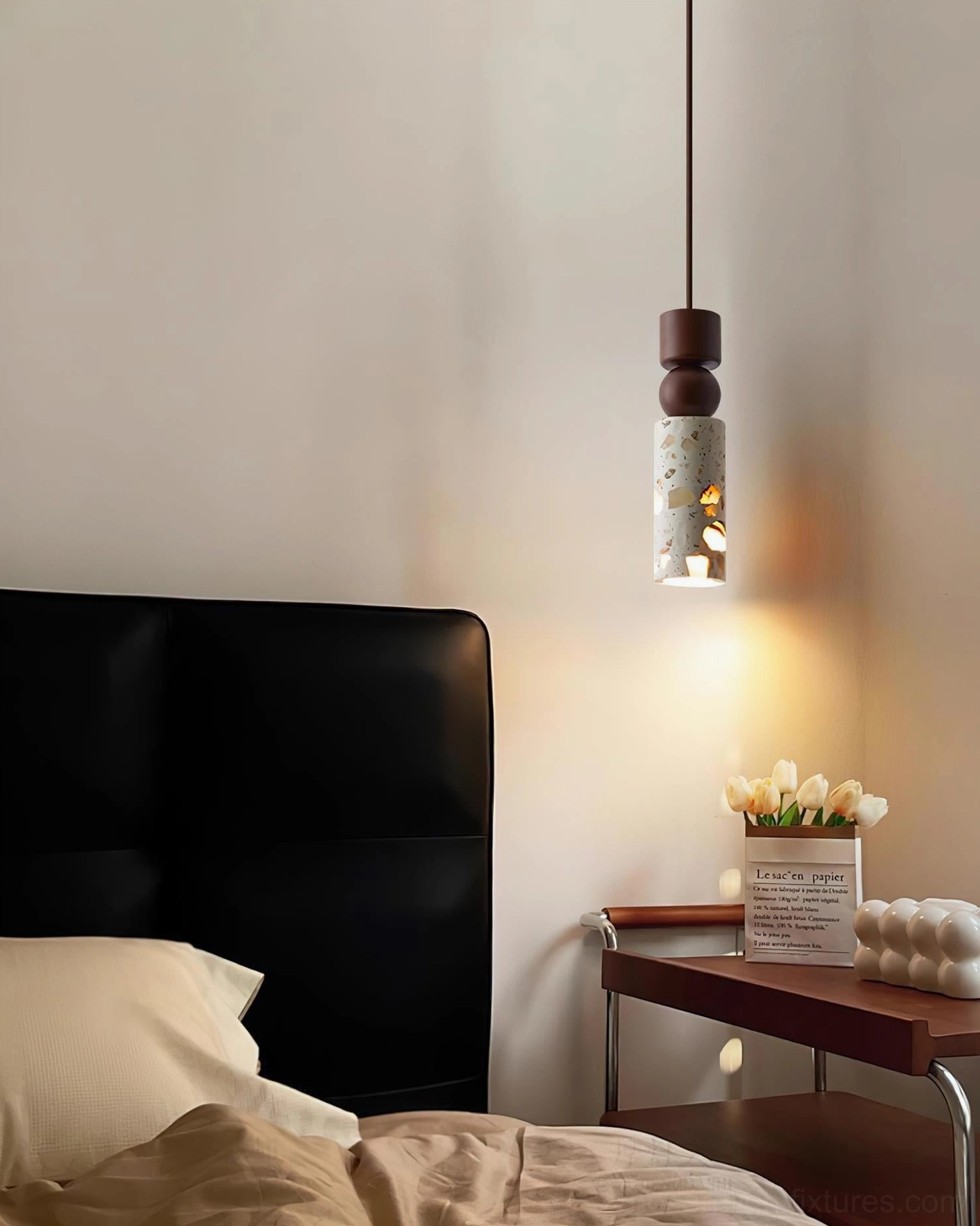Artena hanging lamp beside black headboard with floral decorated side table and warm lighting