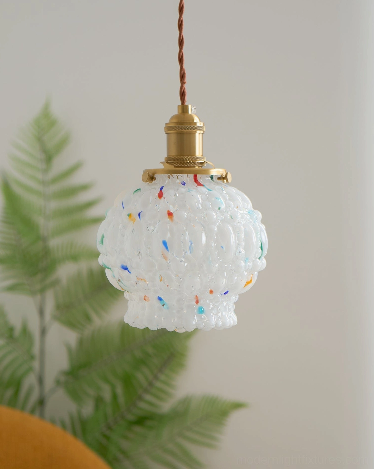 Unlit hand-blown frosted glass pendant light with colorful speckles, brass fitting, boho plant decor corner view