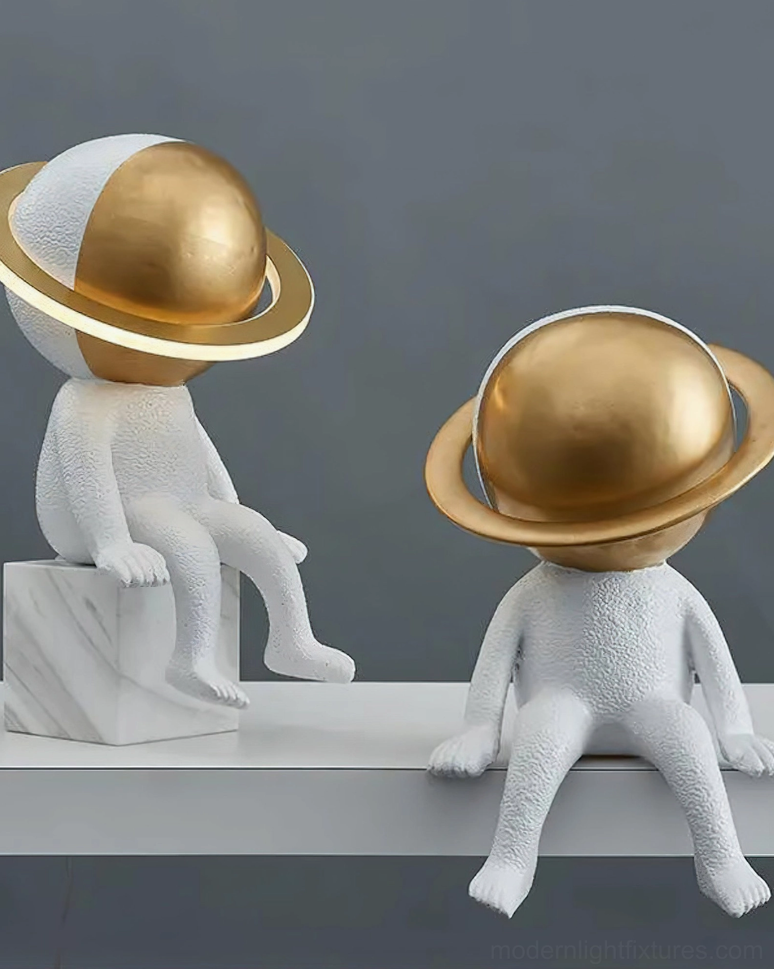 Two modern astronaut table lamps on grey shelf with brass gold planet heads in contemporary minimalist setting