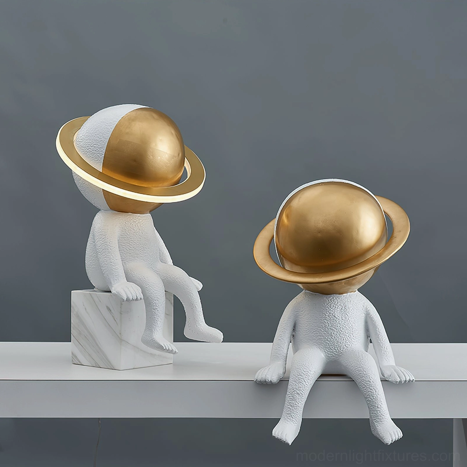 Two astronaut Halo LED lamps on grey shelf showing side profile with illuminated brass gold planet heads