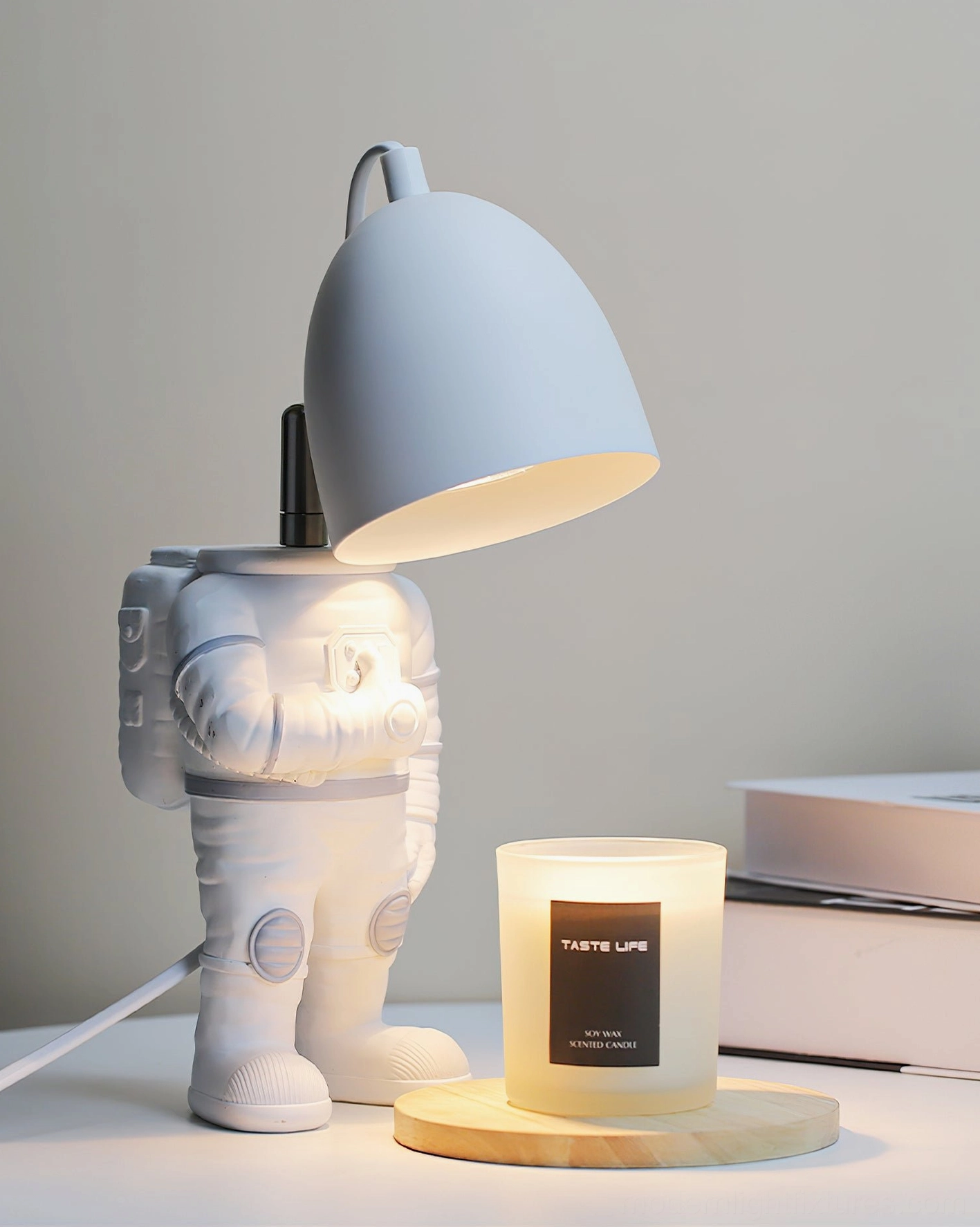 Astronaut candle warmer table lamp three-quarter view on desk with stacked books and warm lighting