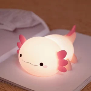 Pink axolotl LED night light with warm glow next to notebook, overhead angle showing feathered gills detail