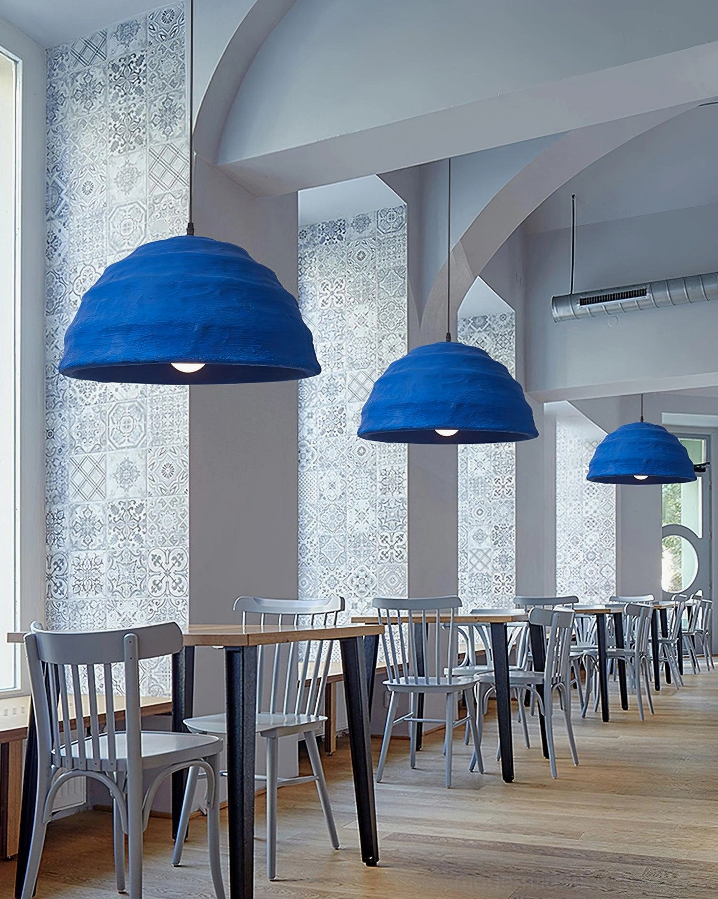 Multiple azure dome pendant lights illuminating spacious bright cafe with wooden furniture ambient lighting