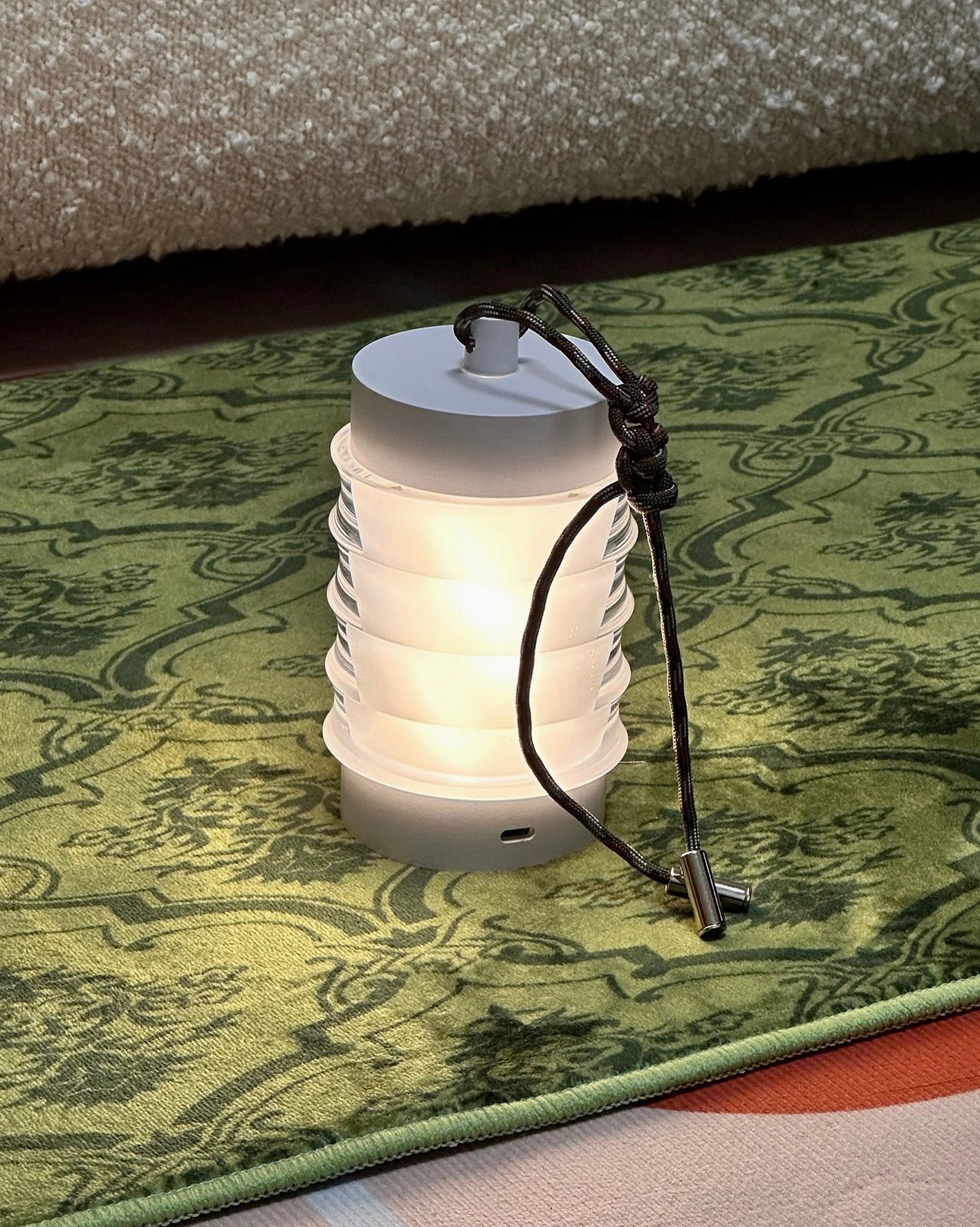 Balia portable table lamp emitting warm glow with black integrated carrying handle, front perspective on vintage area rug backdrop