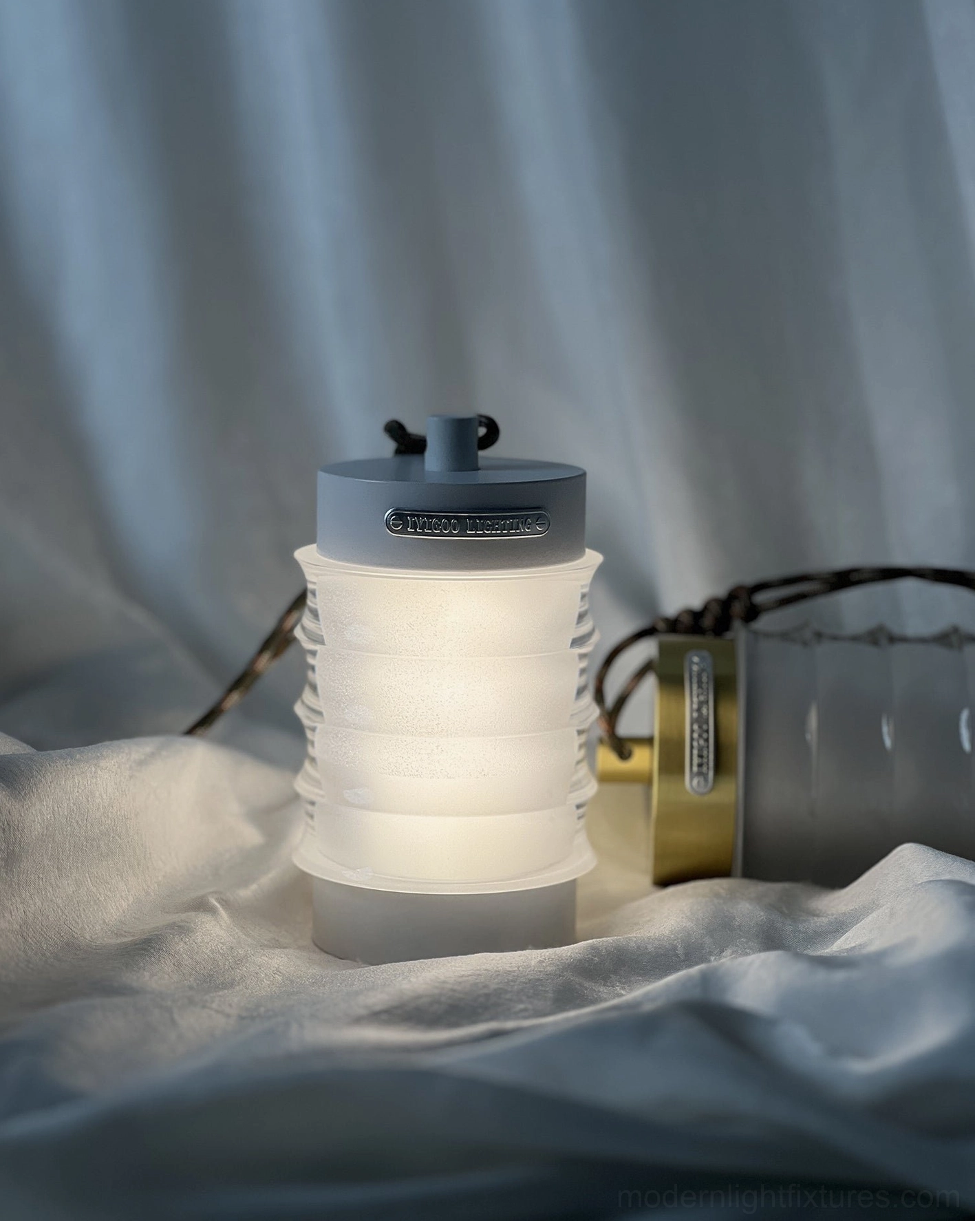 Balia portable LED table lamp emitting warm 3000K glow in bedroom setting with soft draped fabric and gold metallic accents