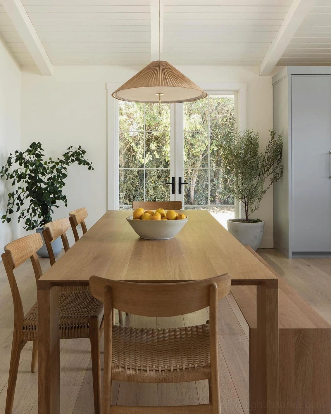 Handwoven bamboo pendant light above bright minimalist wooden dining table, warm brown shade detail