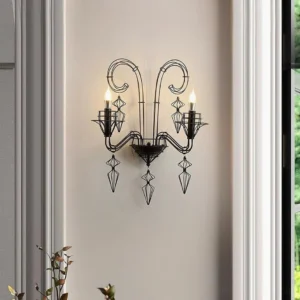 Lit black wrought iron dual-arm wall sconce mounted in modern hallway with gray trim and white walls, showcasing ambient candle-style lighting