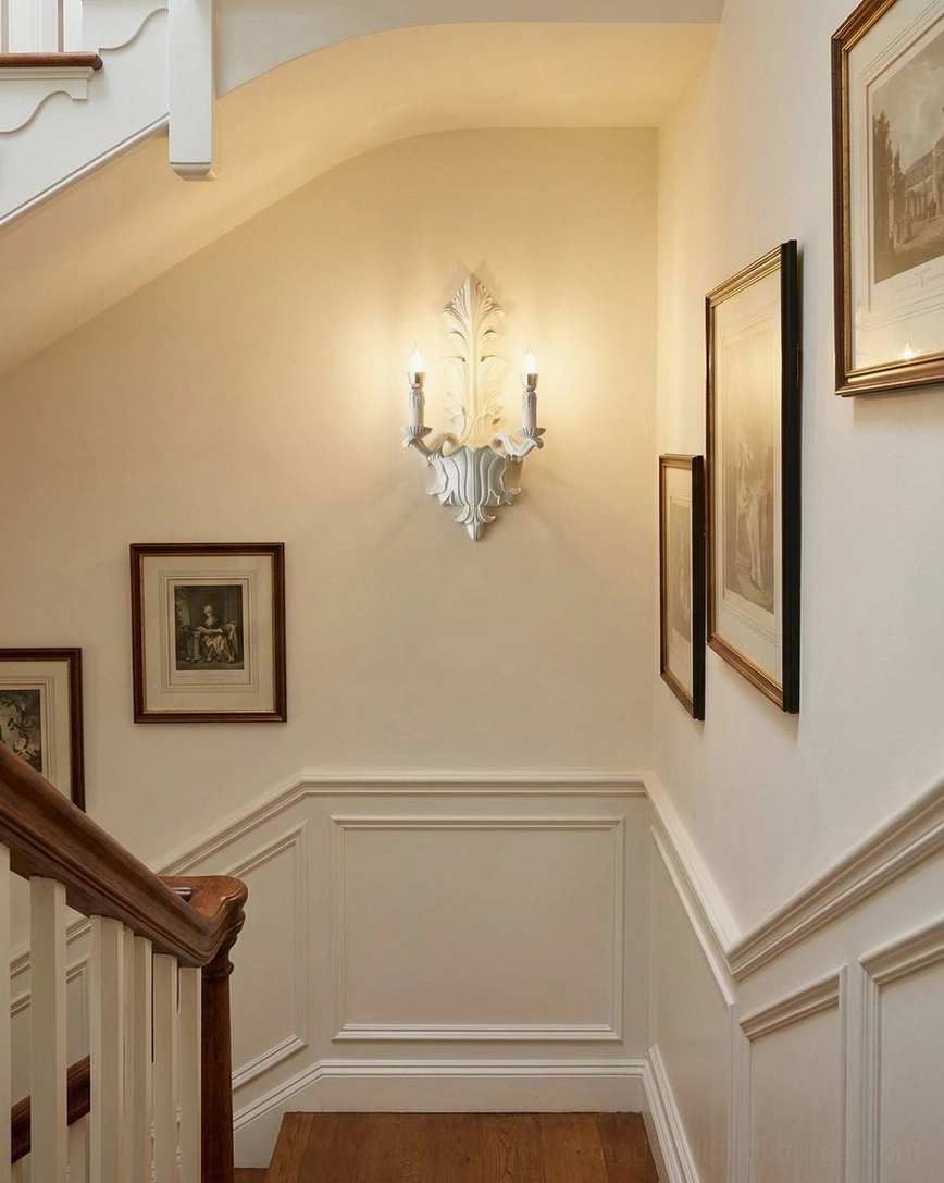 Matte white baroque wall sconce on stairwell wainscoting with framed artwork in residential hallway