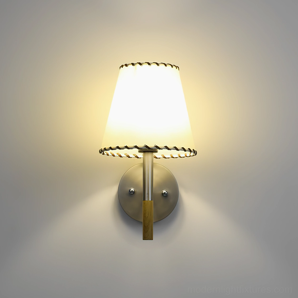 BC2 wall sconce illuminated on warm gray wall showing soft glowing light through hand-stitched shade trim