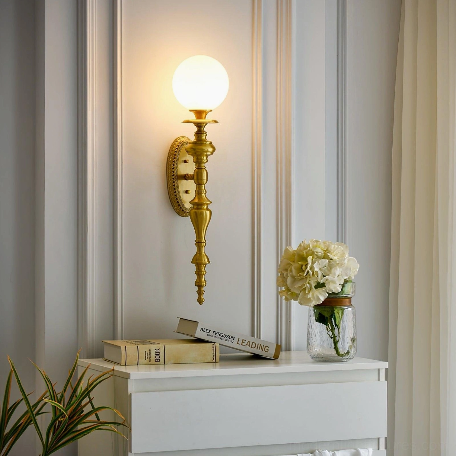 Brass wall sconce mounted above console table in entryway with warm glowing light and home decor