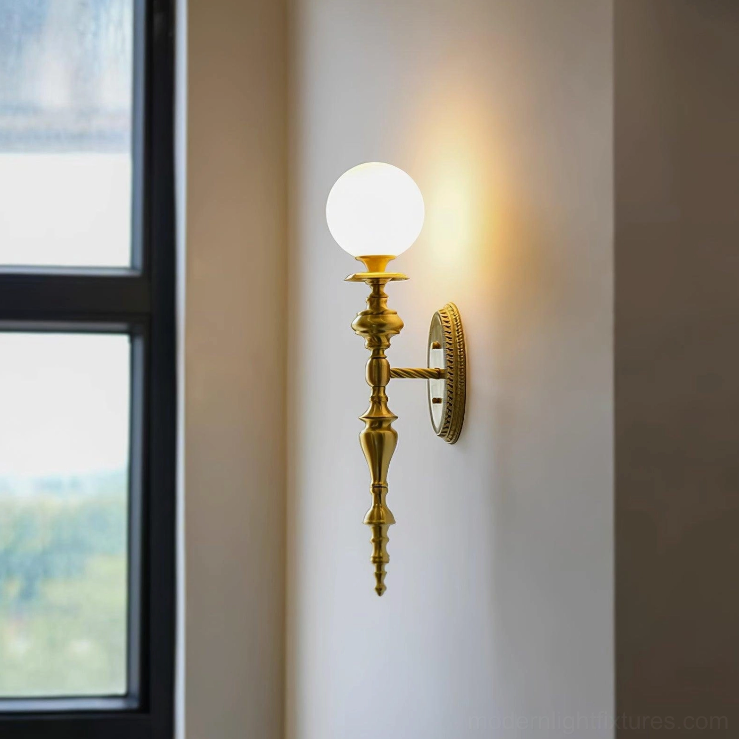Wall mounted brass sconce installed by window with warm ambient light and polished gold hardware