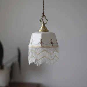 White ceramic pendant lamp with geometric patterns and gold hardware, beaded tassel trim, home interior setting
