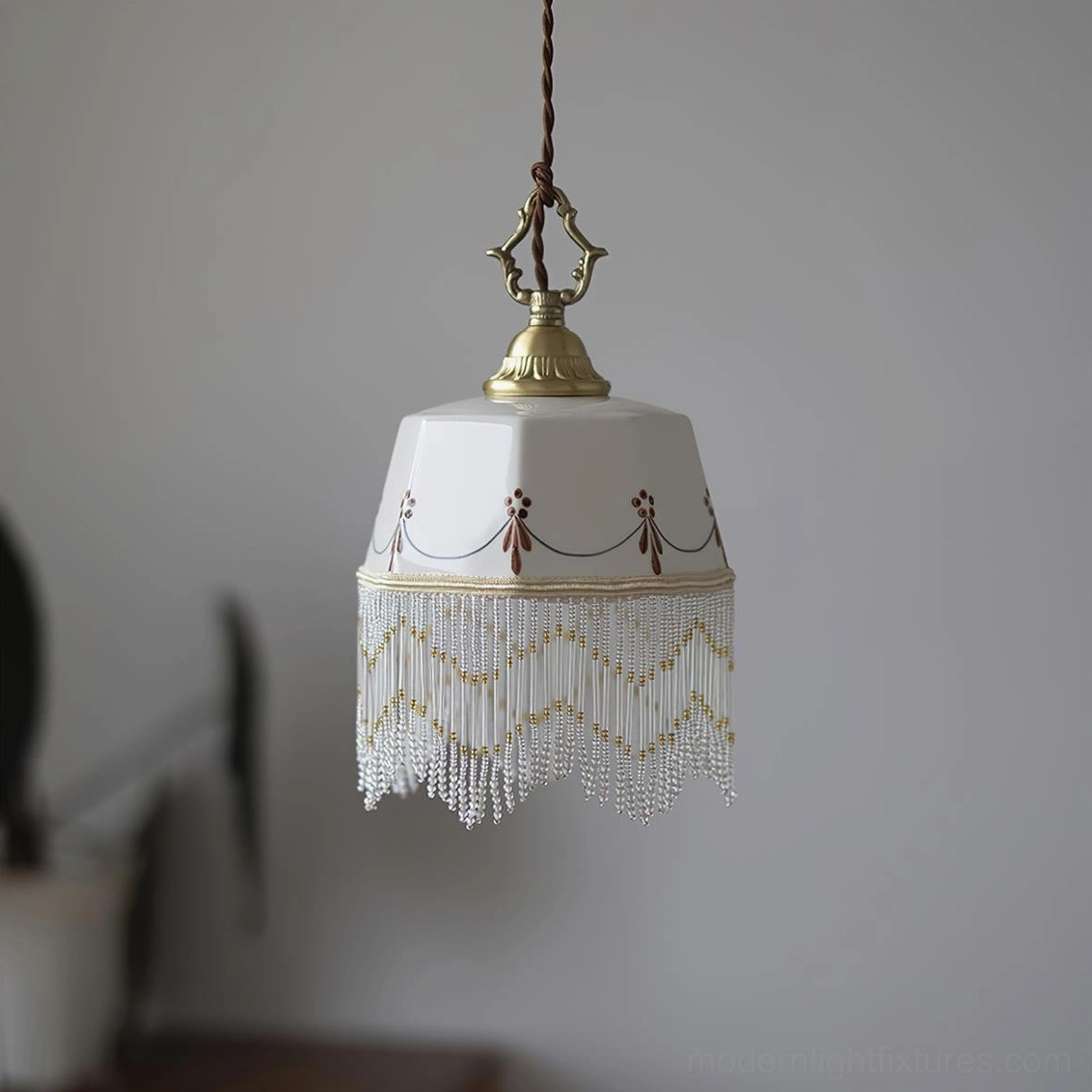 White ceramic pendant lamp with geometric patterns and gold hardware, beaded tassel trim, home interior setting