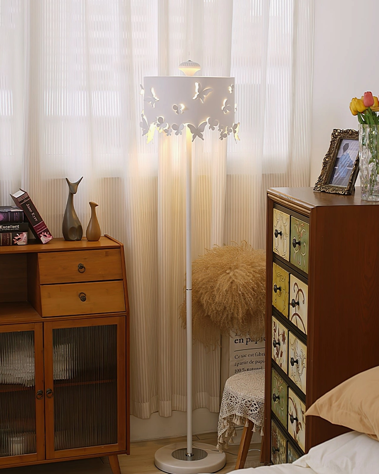 Butterfly floor lamp positioned in vintage bedroom corner near wooden dresser and sheer curtains, soft evening lighting