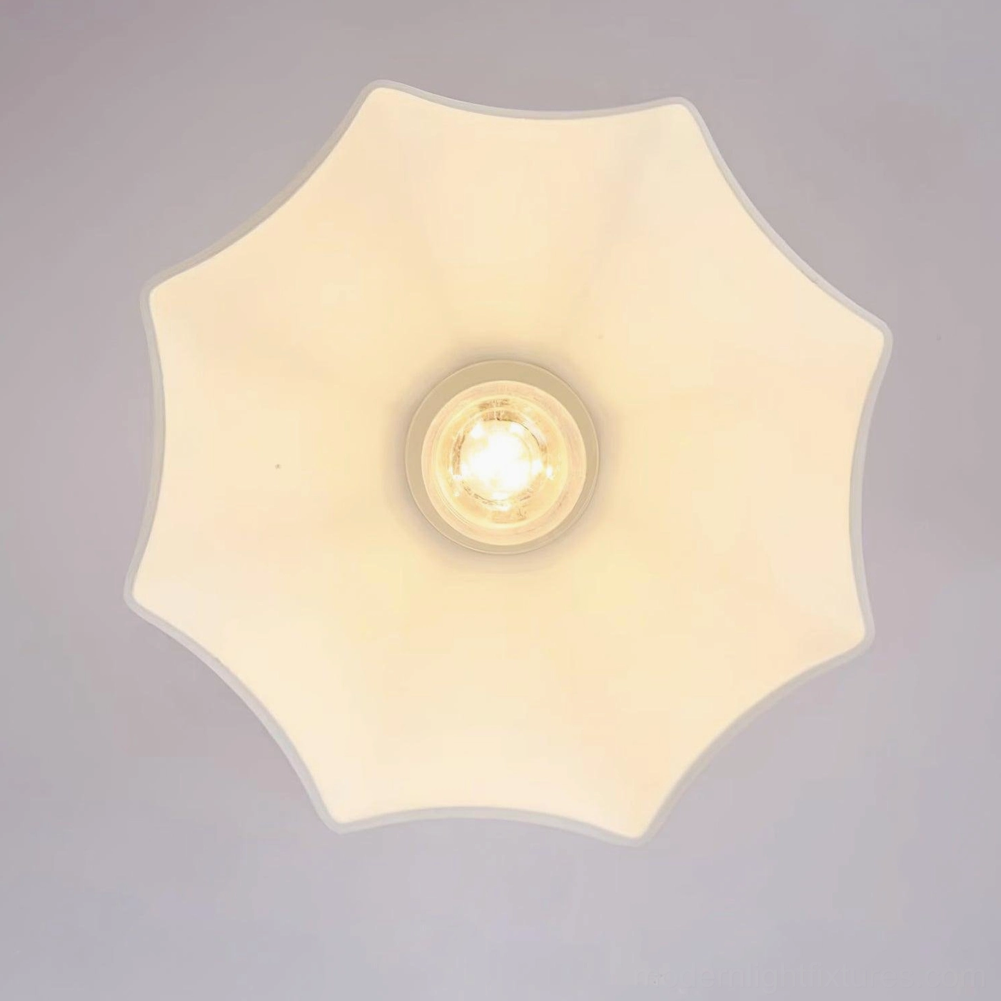 Brass and frosted acrylic scalloped semi-flush light creating warm lighting in bedroom setting