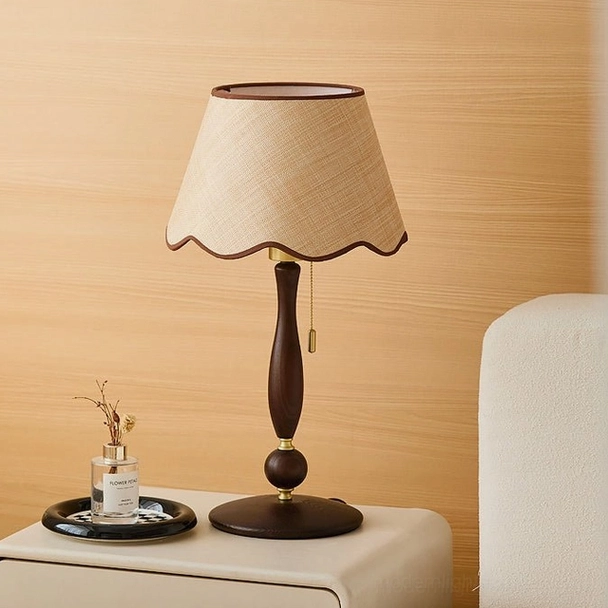 Bedside table lamp with natural cream linen scalloped shade and rich walnut finish wood base placed on nightstand with neutral bedroom decor - three-quarter view