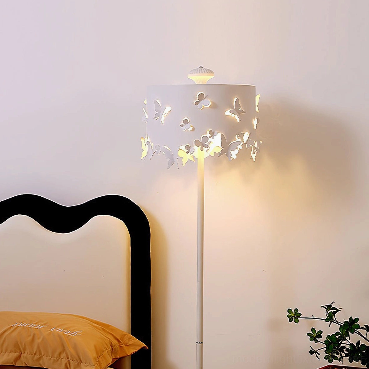 Butterfly floor lamp close-up frontal view in bedroom bedside area, white metal pole with hollow butterfly shade warm lighting