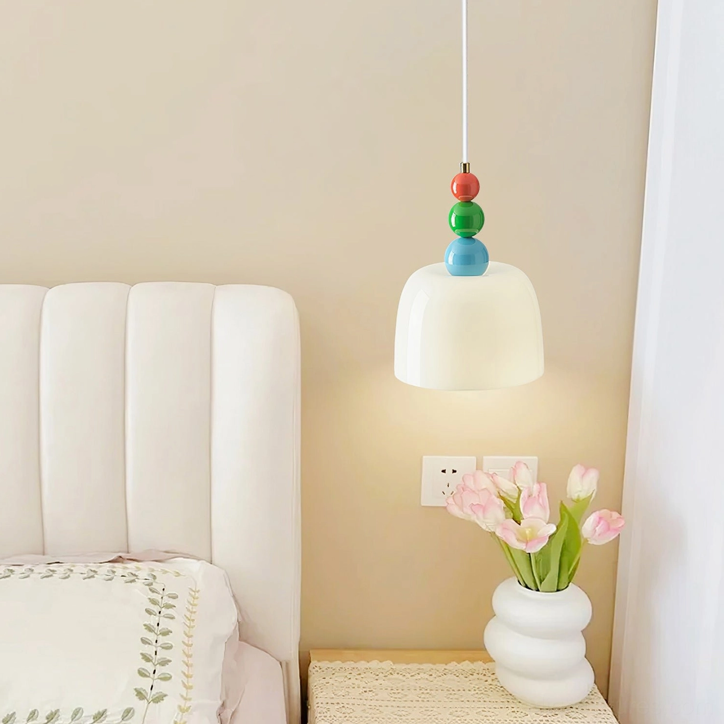 White frosted glass pendant lamp as bedside lighting above tufted headboard with pink tulips
