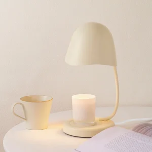 Elegant beige candle warmer lamp on bedside table with candle and ceramic mug home decor