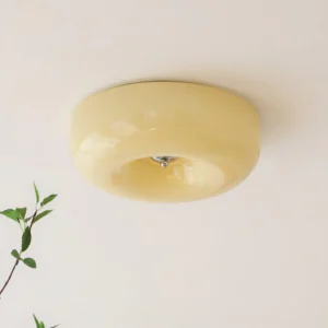Warm beige donut ceiling light fixture mounted on ceiling with green foliage, low-angle upward view