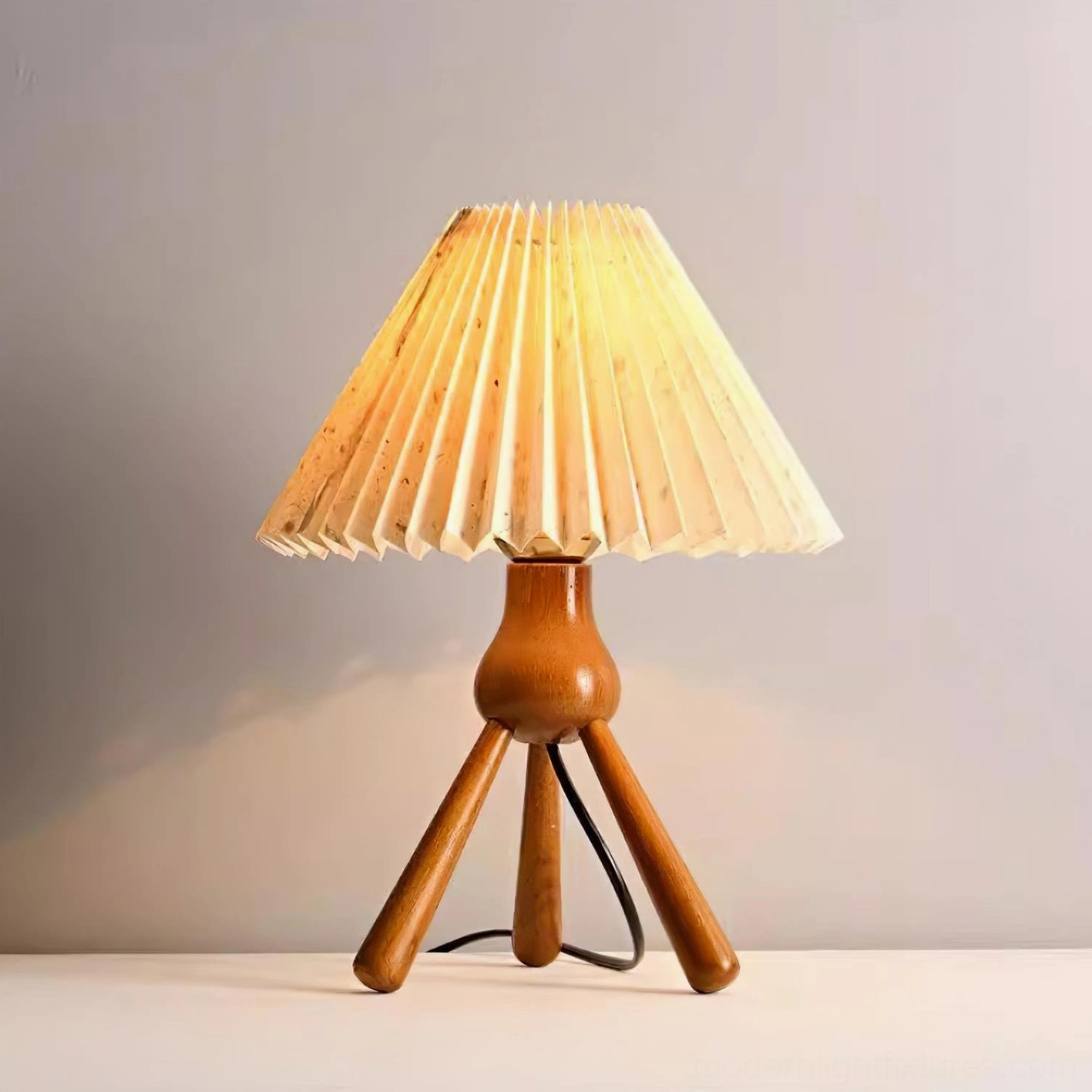 Beige pleated tripod table lamp glowing with warm light, wood base and fabric shade detail