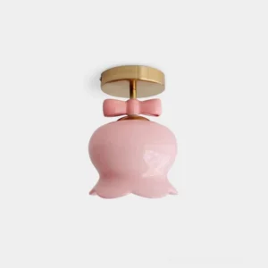 Close-up top-down view of bell-shaped ceiling light with pink glass shade and brass metal base, showing intricate bow knot detail and bell silhouette design